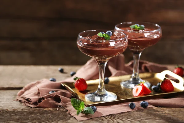 Schokoladendessert in Gläsern und frischen Beeren auf farbigem Holzhintergrund — Stockfoto