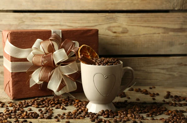 Bonito presente com arco e grãos de café na caneca, no fundo de madeira — Fotografia de Stock