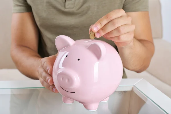 Man puts coin into a piggy-bank — Stock Photo, Image