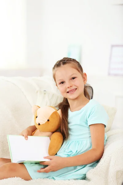 Liten flicka sitter på soffan med bok — Stockfoto