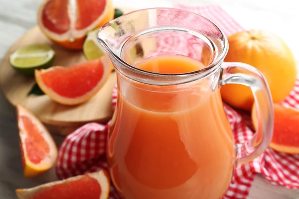 Burk med citrus juice och färsk frukt på ljus trä bakgrund — Stockfoto