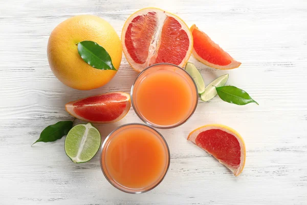 Two glasses of citrus juice and fresh fruits on light wooden background — Stock Photo, Image