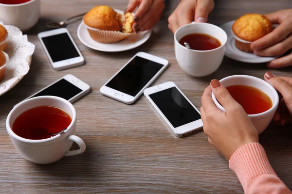 Четыре руки со смартфонами держа чашки с чаем, на деревянном фоне стола — стоковое фото