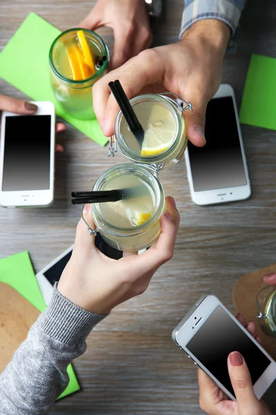 Kokteyller, ahşap masa arka planda tutarak akıllı telefonlar ile dört el — Stok fotoğraf