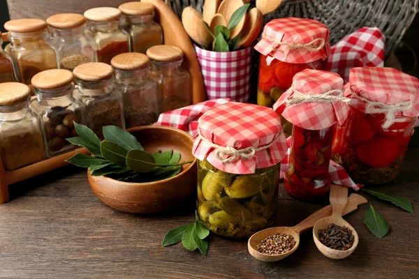 Frascos com legumes em conserva e feijão, especiarias, livro de receitas e utensílios de cozinha sobre fundo de madeira — Fotografia de Stock