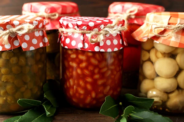 Jars with pickled vegetables and beans on wooden background — Stock Photo, Image