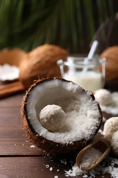 Caramelos en copos de coco, vaso de leche y coco fresco sobre fondo de madera oscura —  Fotos de Stock