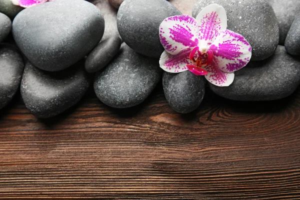 Pedras de spa e orquídea em fundo de madeira — Fotografia de Stock