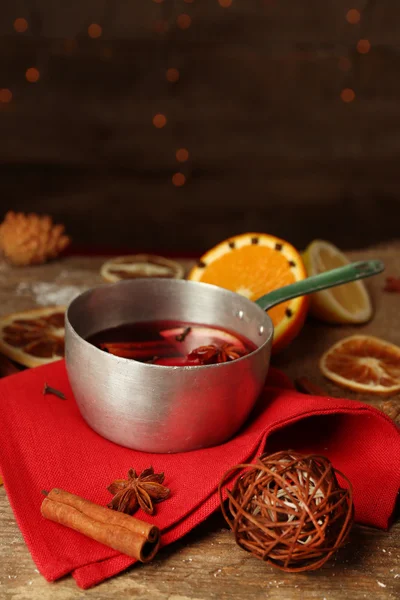 Mulled wine in stew-pan on decorated with red napkin, cinnamon and orange wooden background — Stock Photo, Image