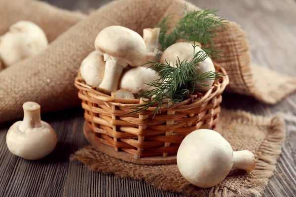 Champignon paddestoelen, een mand, dille en plundering mat op houten achtergrond — Stockfoto