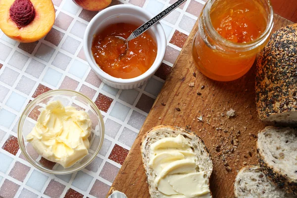 バターとモザイクの背景に木製タブレットの瓶とボウル、熟した桃のパンで美味しいジャム — ストック写真
