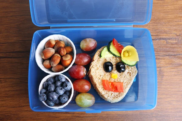 Lunchbox met creatieve sandwich en vruchten op houten achtergrond — Stockfoto