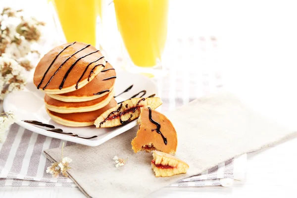 Tasty pancakes with jam on white plate with orange juice and flowers, close up — Stock Photo, Image