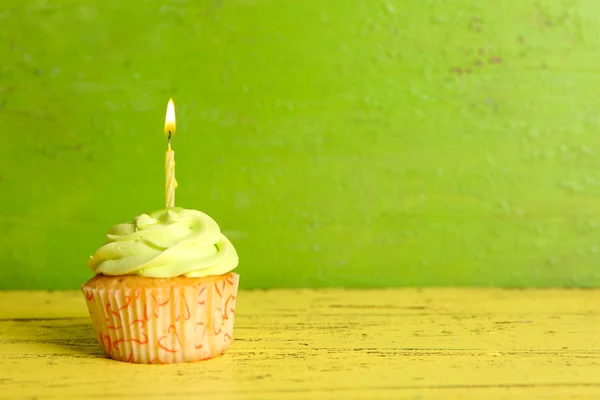 Вкусный кекс со свечой на желтом деревянном столе на зеленом фоне — стоковое фото