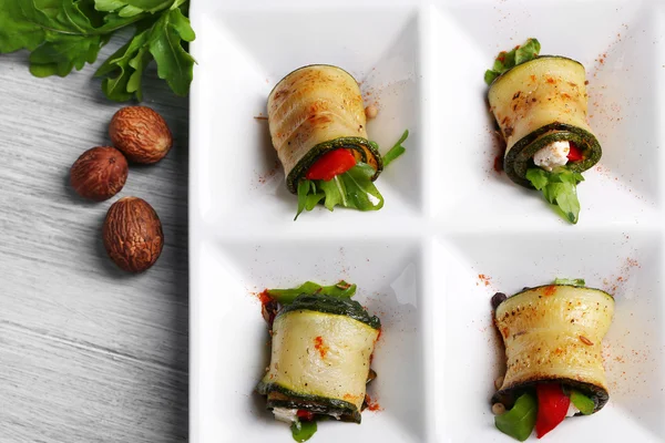 Rollos de calabacín con queso, pimientos y rúcula en el plato, primer plano, sobre fondo de mesa — Foto de Stock