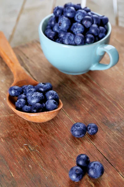Färska blåbär i kopp och sked på träbord nära håll — Stockfoto