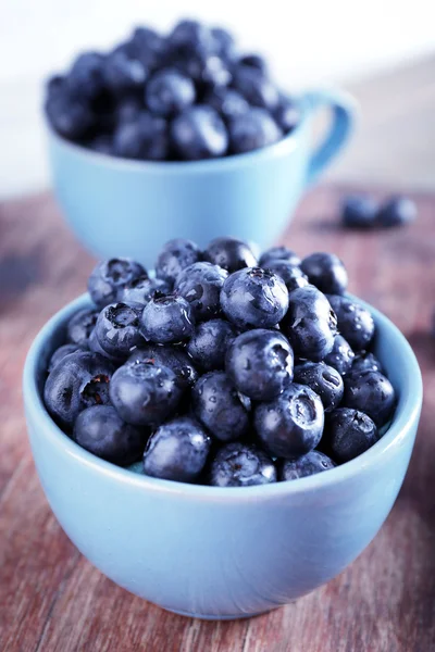 Färska blåbär i koppar på träbord nära håll — Stockfoto