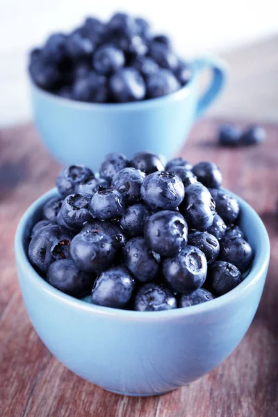 Frische Blaubeeren in Tassen auf Holztisch aus nächster Nähe — Stockfoto