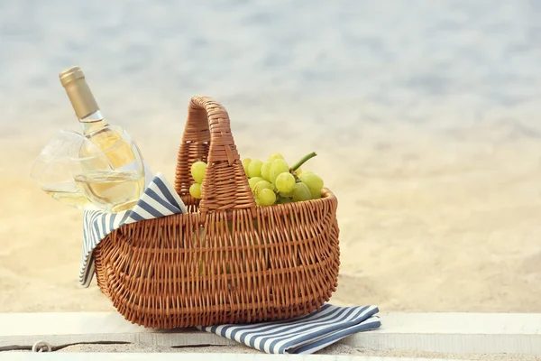 Picnic basket with bottle of wine on sand beach — Stock Photo, Image