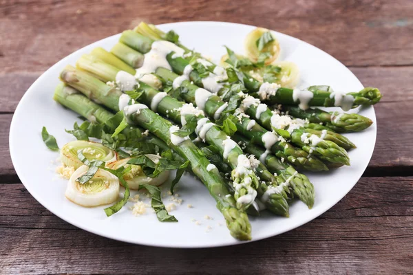 Asperges appétissantes dans une sauce à la crème sure avec oignon et fromage sur plaque blanche sur fond de bois — Photo