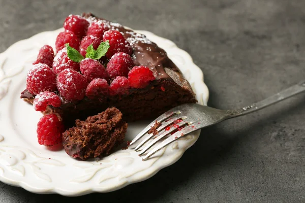 Кусочек торта с шоколадной глазурью и малиной на тарелке на темном фоне — стоковое фото
