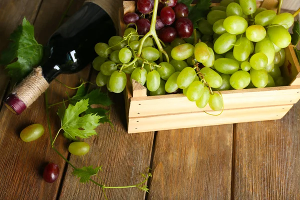 Uva blanca y roja en caja con botella de vino sobre fondo de madera — Foto de Stock