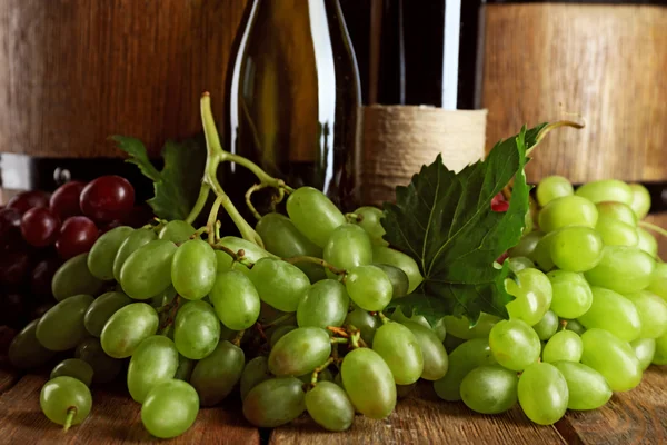 Uva blanca y roja con botella de vino sobre fondo de madera — Foto de Stock