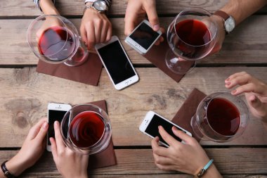 Kırmızı şarap, gözlüklü ahşap masa arka planda tutarak akıllı telefonlar ile dört el