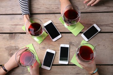 Kırmızı şarap, gözlüklü ahşap masa arka planda tutarak akıllı telefonlar ile dört el