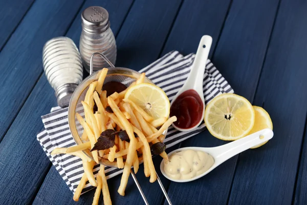 Fransız kızarmış patates soslu ahşap arka plan üzerinde metal kevgir içinde — Stok fotoğraf