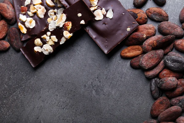 Svart choklad bitar med nötter och Kakao bönor på mörkgrå bakgrund — Stockfoto