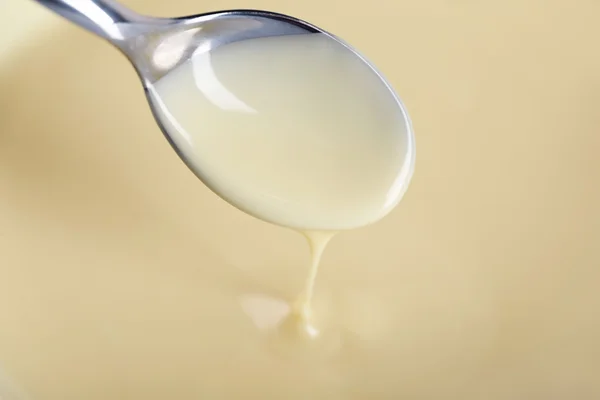 Fondo de leche condensada y una cuchara en un tazón, primer plano — Foto de Stock