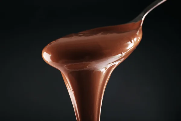 Schokolade auf einem Löffel auf dunklem Hintergrund gegossen — Stockfoto