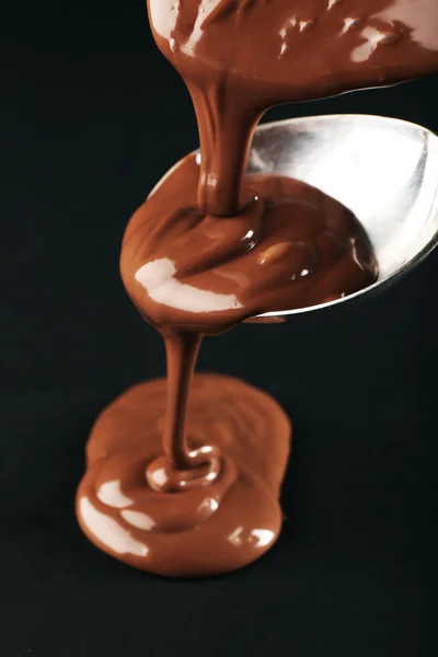 暗い背景にスプーンに注ぎチョコレート — ストック写真