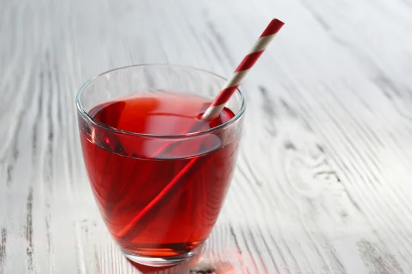 Um copo de suco de granada saboroso com uma palha, no fundo de madeira — Fotografia de Stock