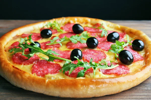 Pizza saborosa com salame e azeitonas na mesa de madeira contra fundo preto — Fotografia de Stock