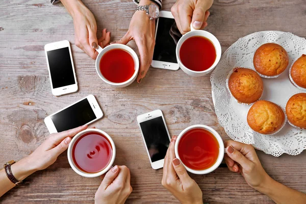 Bardak çay, ahşap masa arka planda tutarak akıllı telefonlar ile dört el — Stok fotoğraf