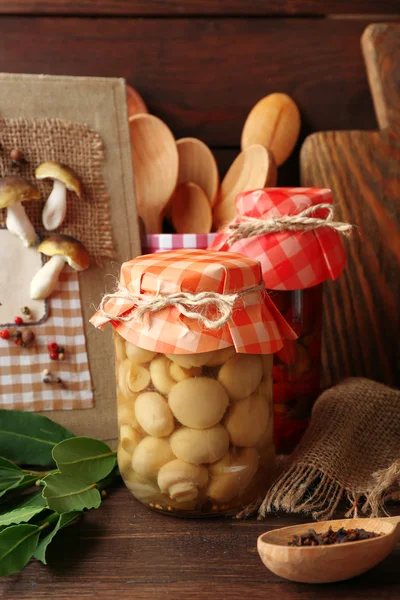 Jars with pickled vegetables, beans, spices and kitchenware on wooden background — Stock Photo, Image