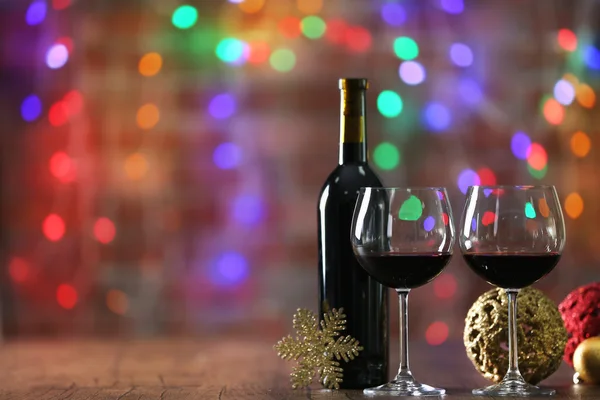 Red wine and Christmas ornaments on wooden table on Christmas lights background — Stock Photo, Image