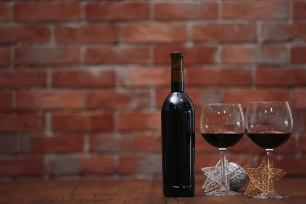 Vino tinto y adornos navideños sobre mesa de madera sobre fondo de ladrillo — Foto de Stock