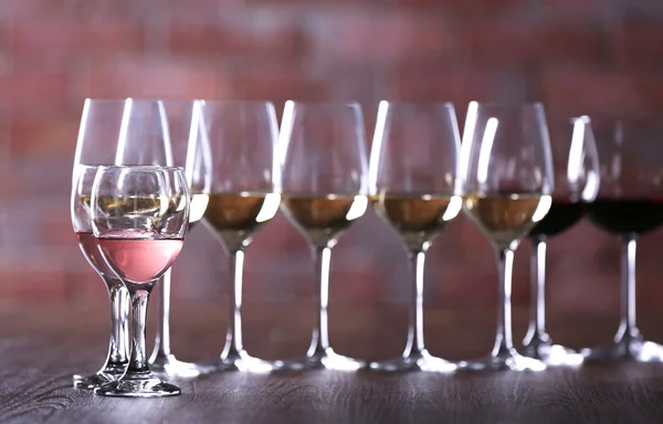 Wijnglazen met wit, rood en roze wijn op houten tafel op muur steen achtergrond — Stockfoto