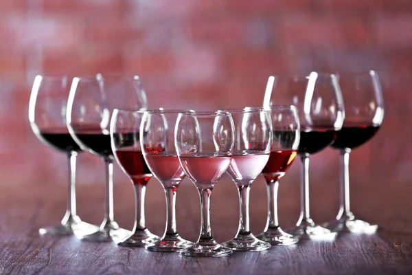 Weingläser mit weißem, rotem und rosa Wein auf Holztisch auf gemauertem Hintergrund — Stockfoto