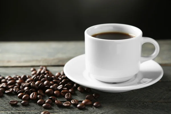 Чашка кофе и зерна кофе на деревянном столе, на сером фоне — стоковое фото