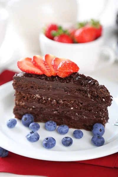 Chocolate cake met chocolade en verse bessen op plaat, op houten tafel, op lichte achtergrond — Stockfoto