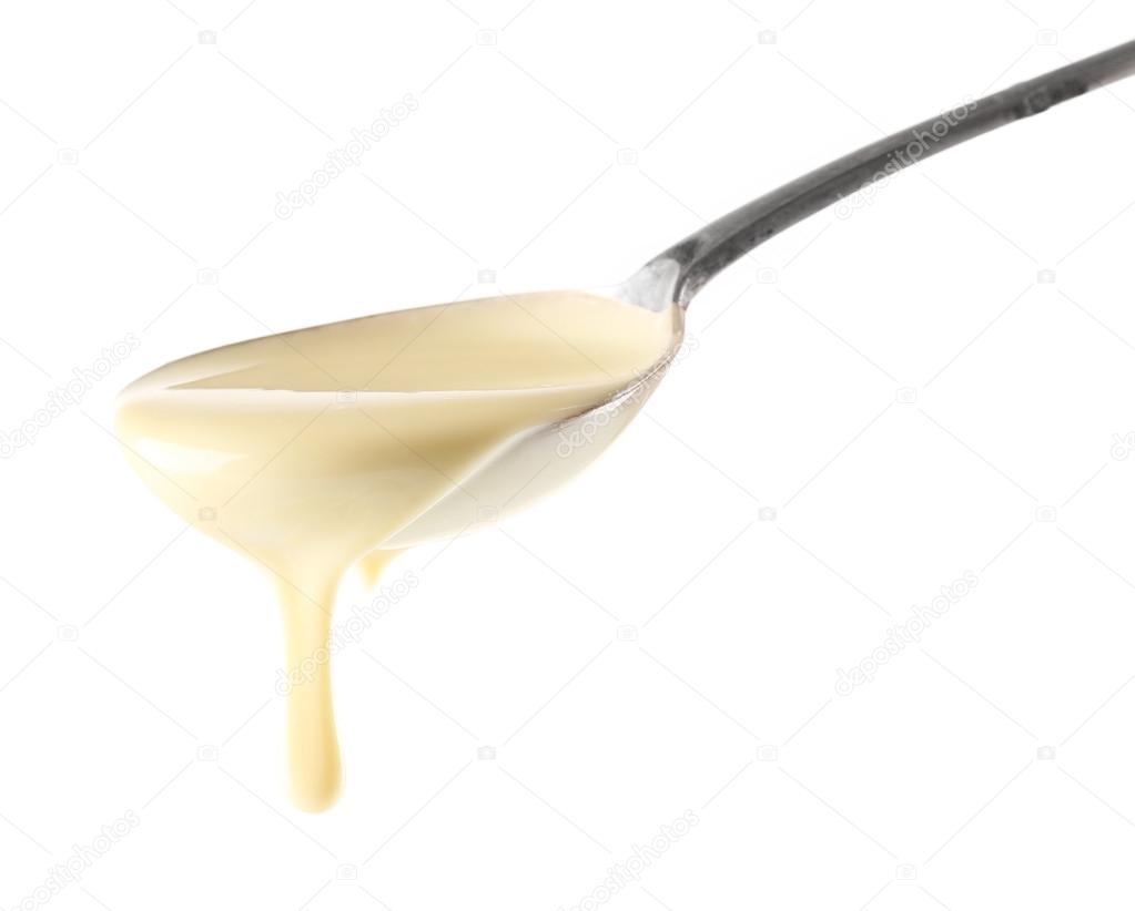 Condensed milk pouring from a spoon, isolated on white Stock Photo by