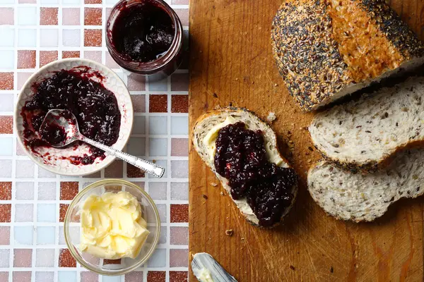 Selai lezat di piring, mentega, roti segar dan tablet kayu dengan latar belakang mosaik — Stok Foto