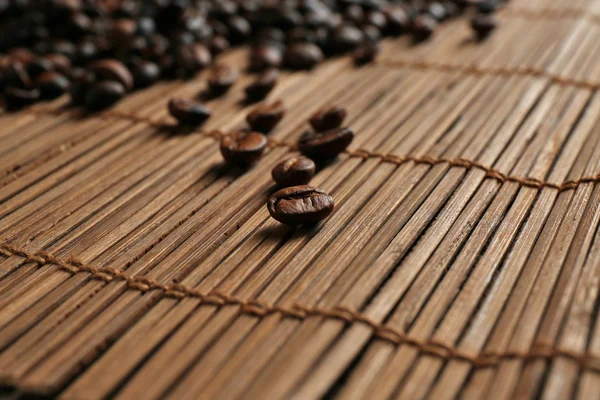 Aromatic coffee beans scattered on bamboo mat — Stock Photo, Image
