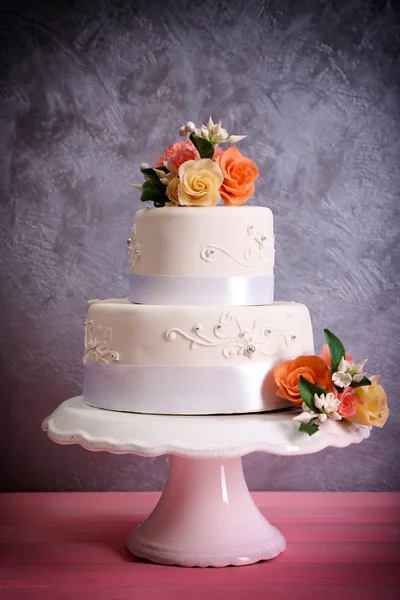 Bílé svatební dort zdobený květy růžové dřevěný stůl proti šedé pozadí — Stock fotografie