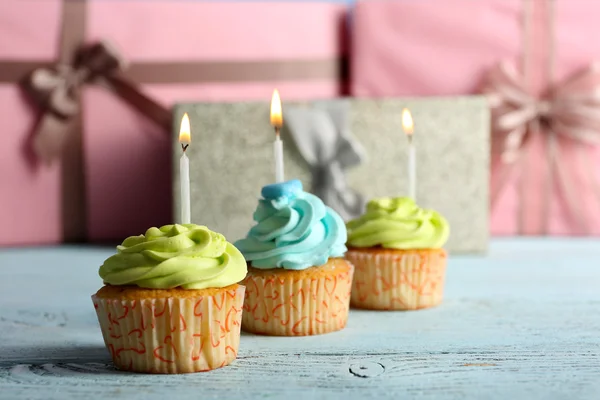 Delicious cupcakes with candles on violet table against wooden background — Stock Photo, Image