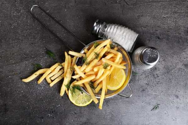 Franse frietjes met citroen en zout in zeef op tafel — Stockfoto